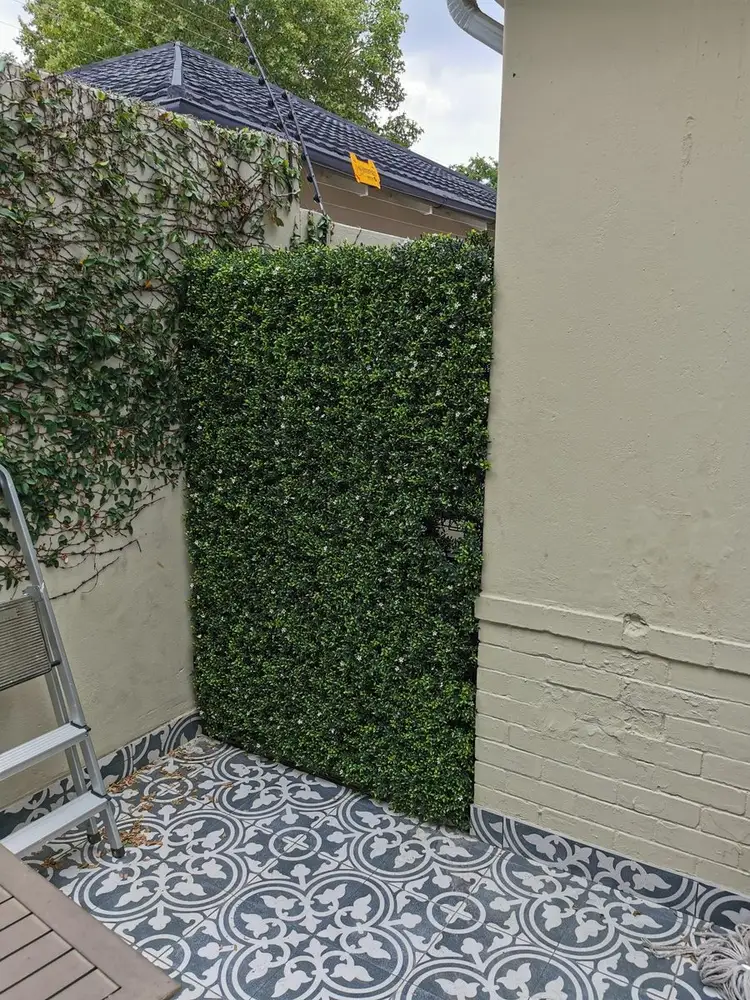 Corner screening beside patterned paving: Tall hedge panels wrap a small courtyard corner next to decorative stones and paving.