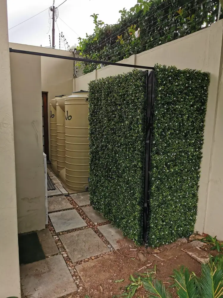 Narrow side-passage privacy screen: A freestanding green screen closes off the end of a narrow passage beside the house.