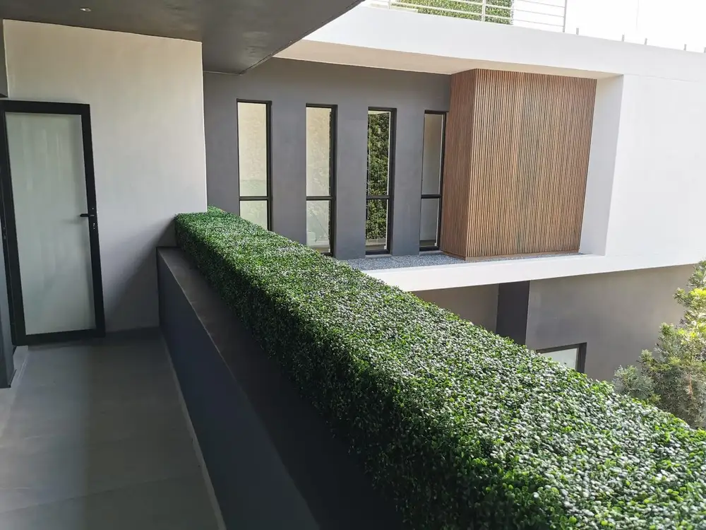 Balcony planter-edge hedge: A low, continuous hedge runs along the raised planter edge beside a modern balcony walkway.